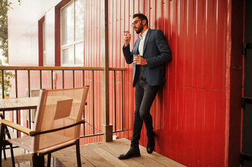Handsome well-dressed arabian man smoke cigar with glass of whiskey at balcony of pub.
