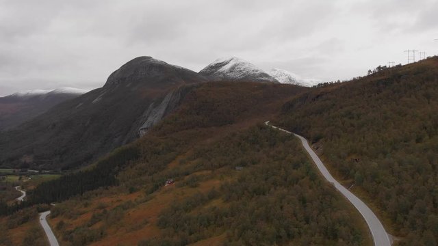Aerial shot of a road ascending up towards a snow capped mountains in the background. Eresfjord, Norway.