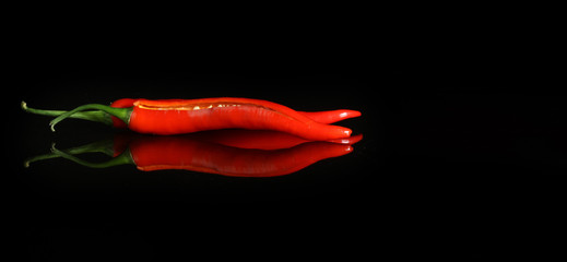 black background with red hot pepper and reflection