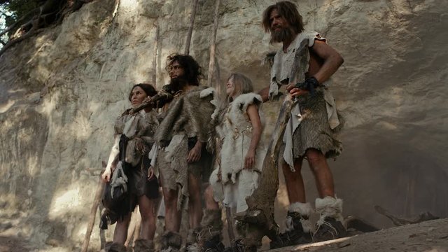 Tribe of Hunter-Gatherers Wearing Animal Skin Holding Stone Tipped Tools, Stand Near Cave Entrance.. Neanderthal Family Ready for Hunting in the Jungle or Migratiion