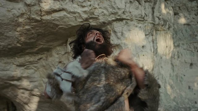 Portrait of Primeval Caveman Wearing Animal Skin Does Aggressive Chest Beating and Screaming, Defending His Cave and Territory in the Prehistoric Forest. Prehistoric Neanderthal or Homo Sapiens Leader