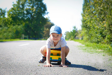 A boy in a baseball cap playing on an asphalt road with a large truck