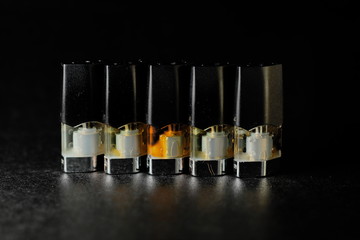 e-juice vape refill pods with liquids of different shades of orange yellow, black background isolated close up