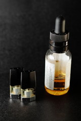 e-juice vape refill pods with with a bottle of orange e-liquid, isolated close up black background