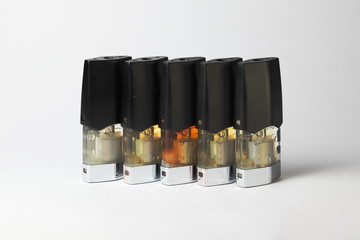 e-juice vape refill pods with liquids of different shades of orange yellow, white background isolated close up