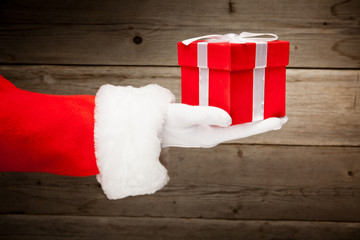 Obraz na płótnie Canvas Santa hand holding a red gift box against wooden background