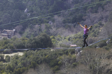 A woman is walking along a stretched sling. Highline in the mountains. Woman catches balance. Performance of a tightrope walker in nature.