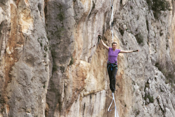 A woman is walking along a stretched sling. Highline in the mountains. Woman catches balance. Performance of a tightrope walker in nature.