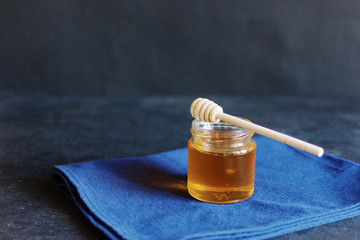 Honey in jar with honey dipper on black color background.