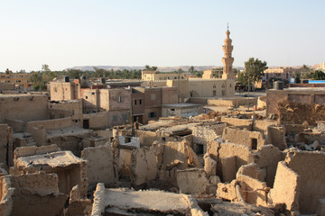 Typical residential district with collapsing huts and houses in the foreground and a minaret tower rising in the background in Siwa, Siwa Oasis, Egypt
