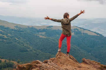Obraz premium A young girl tourist stands with his hands up in happiness from on top of the mountain and enjoys a view of the Carpathian mountains at sunrise.