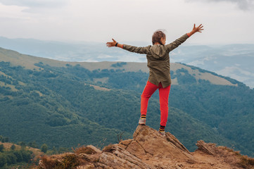 A young girl tourist stands with his hands up in happiness from on top of the mountain and enjoys a view of the Carpathian mountains at sunrise.