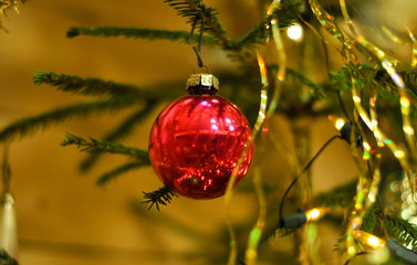 Glass red ball on a Christmas tree among branches, shiny tinsel and electric garlands