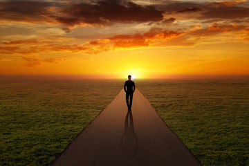 Man walking alone on a road towards the sunset