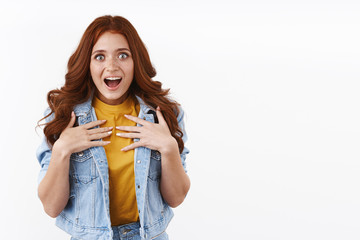 Surprised grateful cute astonished redhead girl with long red curly hairstyle, hold hands on chest from awe and amazement, open mouth gasping flattered and happy, stare camera impressed