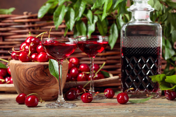 Cherry liquor and red cherries in a wooden bowl on a wooden table in garden.