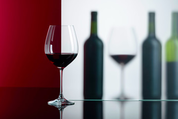 Bottles and glasses of red wine on a black reflective background.