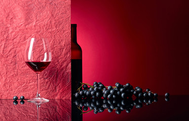 Bottle and glass of red wine on a black table.
