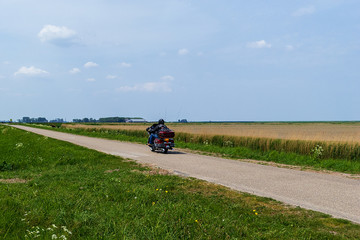 Motorcyclist riding on a country road through the cornfields. Groningen, Netherlands, Europe.