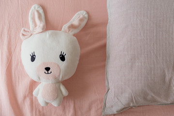 Fototapeta premium View from above on cute rabbit toy with long ears lying on pillow. Kids toy alone in bed at morning time. Concept of girlhood and children.