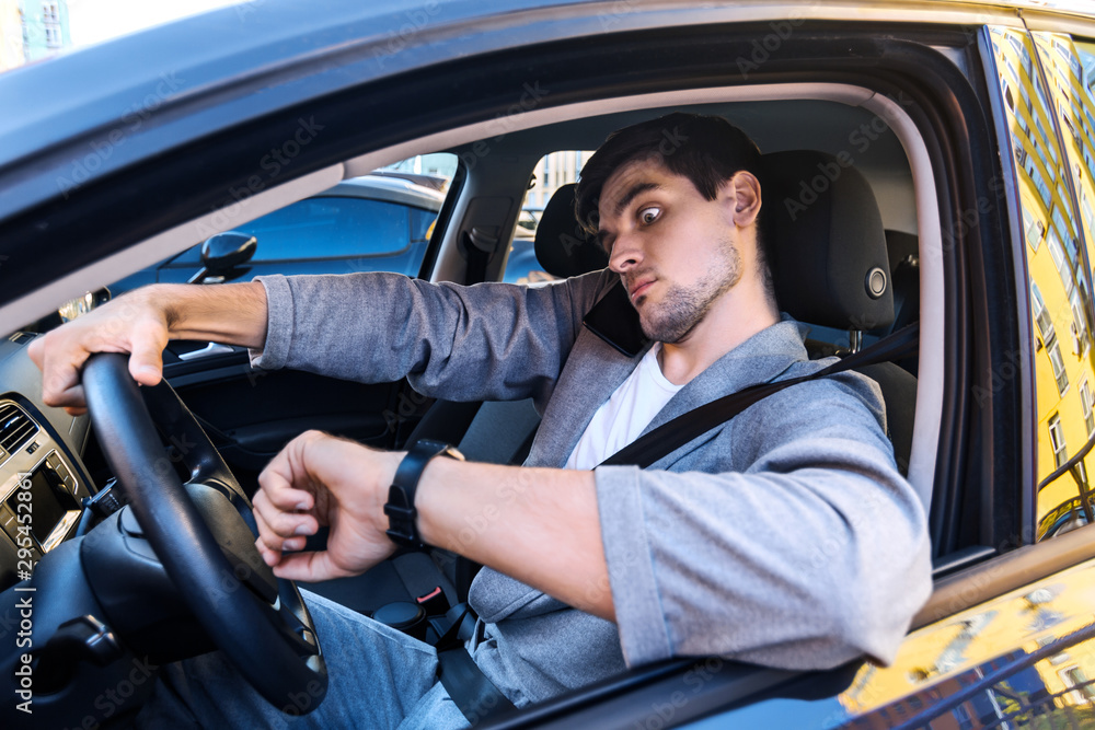 Wall mural annoyed tired young man is riding driving car. businessman is late for meeting. driver brunette in g