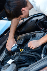 Young brunette man is changing oil in auto with open hood. Driver is repairing automobile on street road. Vehicle breakdown on way concept. Repairman mechanic is servicing car in workshop.