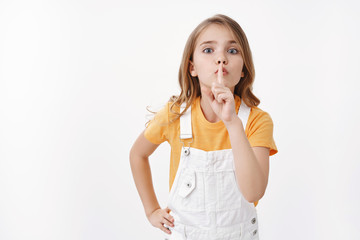 Keep quiet please. Determined obedient cute blond girl child showing hush sign, shushing asking...