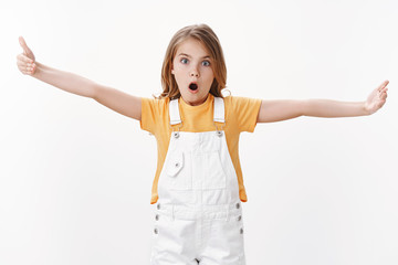 Impressed fascinated cute clever blond girl explain something big, stretch hands showing huge enormous vast product, open mouth and stare camera thrilled, standing speechless white background