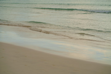 Gentle waves on the beach in the morning. Fading footprints in the sand in warm pastel colors. Atmospheric concept background for travel, tourism and recreation.