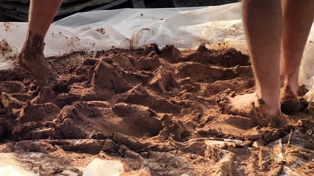 Close up shot of Barefoot clay Kneading for building simple house of adobe airbricks