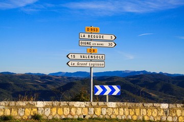 View on white isolated direction signs arrow with endless valley and stone wall against blue sky -...