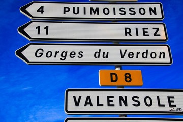 Low angle view and close up of white isolated direction signs arrow against blue sky - Provence, France, (Gorges du Verdon, Puimoisson, Riez, Valensole)