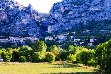View over green valley on French village with giant mountain face background in early morning - Moustiers Sante Marie, Provence, France