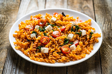 Pasta with tomatoes and white cheese on wooden table