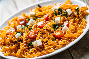 Pasta with tomatoes and white cheese on wooden table