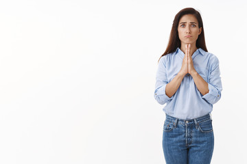 Uneasy cute innocent adult brunette woman asking apology, hold hands pray, pull sad gloomy face, frowning begging mercy, pretty please, asking favor, need lend money, stand white background