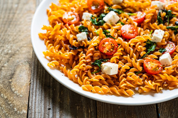 Pasta with tomatoes and white cheese on wooden table
