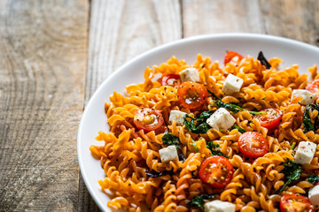 Pasta with tomatoes and white cheese on wooden table
