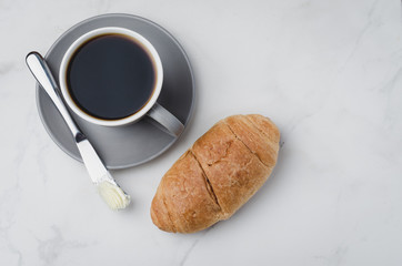 Coffee break with croissant butter knife and cup of black coffee on a white stone table. Top view and copyspace