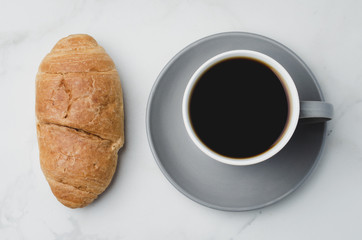 Coffee break. Grey cup with black coffee and croissant on white stone background. Top view