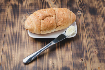 Croissant and a knife with butter on a wooden table. French breakfast