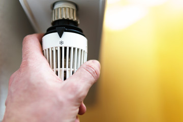 Hand of man adjusting radiator thermostat valve to snow flake frost icon, symbol for saving money...