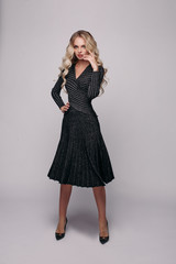 Studio portrait in full length of stunning blonde Caucasian model with long wavy hair wearing beige skirt and blouse and black heels posing in motion with a bag in hand. Isolate. Fashion portrait.