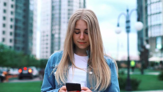 Kyiv, Ukraine - June 5, 2019: beautiful teenage millenial girl using smartphone on the modern city street skycrapers texting sharing messages on social media enjoying mobile technology relaxing in