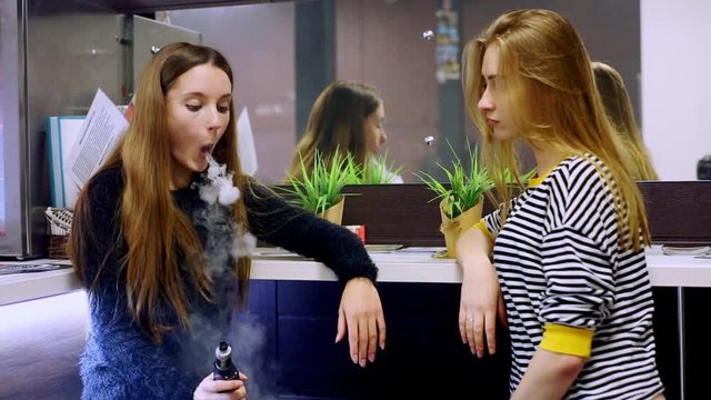 Vape lgbt teenagers. Bisexual lesbian young caucasian teenage girls smoking an electronic cigarette in vape bar. Bad habit that is harmful to health. Young pretty white caucasian teens vaping indoors.