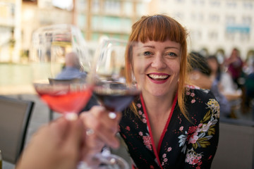 Caucasian redhead woman with floral dress smiling and making toast with red wine