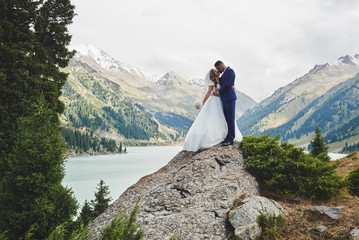 Beautiful wedding photo on mountain lake. Happy Asian couple in love, bride in white dress and...