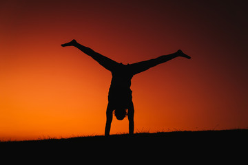 silhouette of young man in a park doing yoga sport. orange sky background. healthy lifestyle.