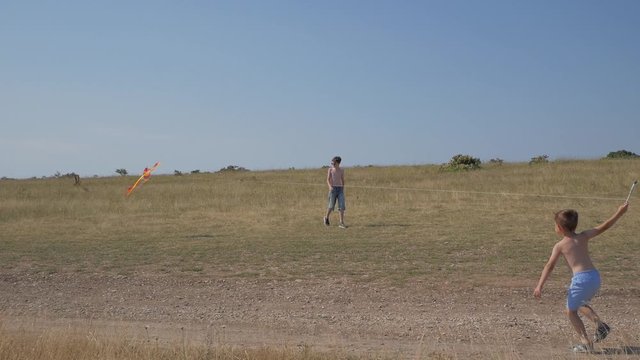 A boy runs along the road with a kite. Dream of flying, children's game. Boys on a background of blue sky. No color grading