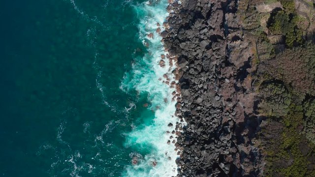 Road on a rocky sea shore. Blue ocean waves break on stones into white foam. Faial, Azores